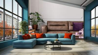 Real photo of modern lamp hanging above leather couch with purple pillow in bright living room interior with coffee table, molding on wall and fresh plant Wall mural