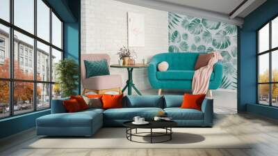 Real photo of turquoise couch and pastel pink armchair standing in bright living room interior with flamingo poster on brick wall and leafy wallpaper Wall mural