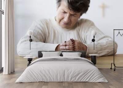 Religious senior woman praying with red rosary in the church. Focus on the hands Wall mural