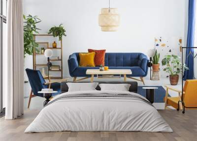 Retro armchairs with wooden frame and colorful pillows on a navy blue sofa in a vibrant living room interior with green plants. Real photo. Wall mural