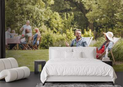 Smiling man with beer talking with friend while relaxing on sunbeds in the garden. Real photo Wall mural