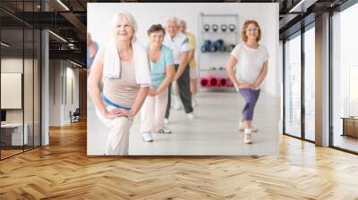 Smiling senior woman with towel exercising during fitness classes for elderly people Wall mural