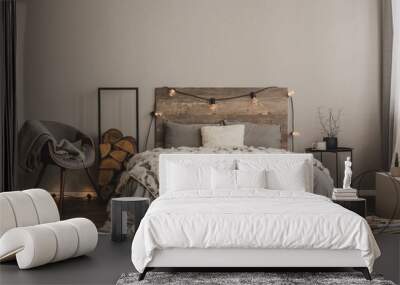 Stylish grey chair with blanket and log of wood next to warm double bed with wooden headboard and light bulbs Wall mural