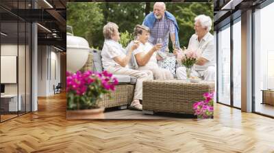 Two senior couples having a social gathering outside on a patio in the garden on summer afternoon. Making a toast. Wall mural