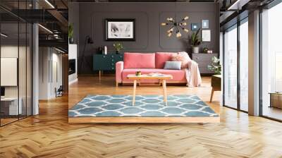 Wooden table on blue carpet in grey living room interior with fireplace and pink sofa. Real photo Wall mural