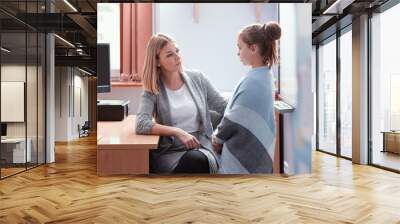 Young beautiful teacher sits at a desk in class and talks to a new student Wall mural