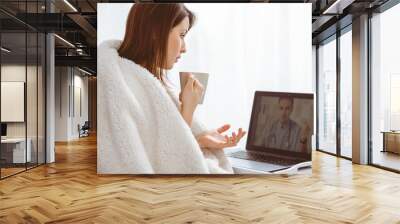 Young woman explaining symptoms of her disease to a doctor over a internet conversation Wall mural