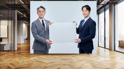 A young office worker man wearing a suit and glasses and a middle-aged man are holding a white board together and posing with various confident expressions and poses. Wall mural