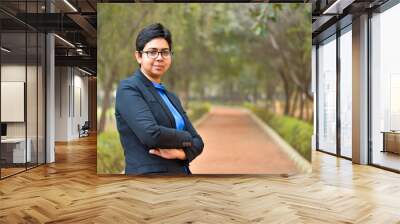 Closeup portrait of a confident young Indian Corporate professional woman with short hair and spectacles, crossed folded hands in an outdoor setting wearing a black business / formal suit Wall mural