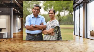 Happy looking retired senior Indian man and woman couple smiling and posing with hands crossed in a park outdoor setting in Delhi, India. Concept love Wall mural