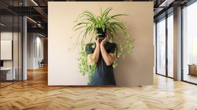 Man standing in front of a brown (beige) wall, holding a spider plant in front of his face Wall mural