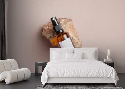 Amber glass spray bottle with white blank label on rock stone on beige background. Natural organic cosmetic product mockup. Flat lay, top view. Wall mural