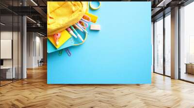 Colorful Back to School Concept. Yellow backpack with various school supplies, including pencils, scissors, an eraser, paper clips, and a ruler on light blue background. Flat lay, top view. Wall mural