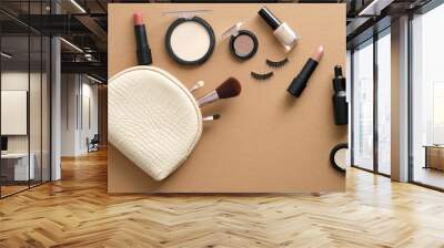 Makeup bag with cosmetic products spilling out on to brown table. Stylish make up artist pouch with beauty products. Flat lay, top view Wall mural