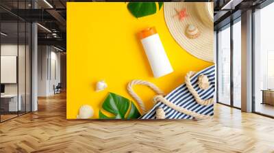 Top view suntan cream bottle, beach bag, female hat and tropical leaves on yellow background. Sun protection on summer vacation concept Wall mural