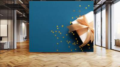 White gift box with golden ribbon bow, fir branches decorated balls and confetti on blue background. Christmas banner mockup, header template. Wall mural