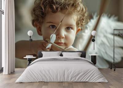 A little boy Cupid with wings aims an arrow of love from a bow. Funny child looking like an angel . Wall mural