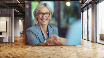 Caucasian smiling middle-aged business woman with a welcoming handshake symbolizes a completed deal, successful negotiations being in the office Wall mural