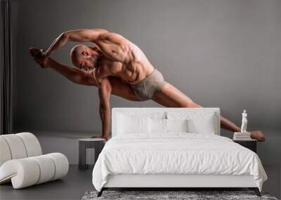 Athletic male dancer performing splits and holding foot in studio Wall mural