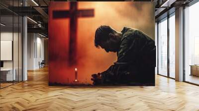 Devout christian man kneeling and praying before a cross in a contemplative atmosphere Wall mural