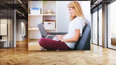 Smiling young woman looking on your laptop sitting on sofa at ho Wall mural