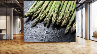 Raw green asparagus on wet black slate background Wall mural