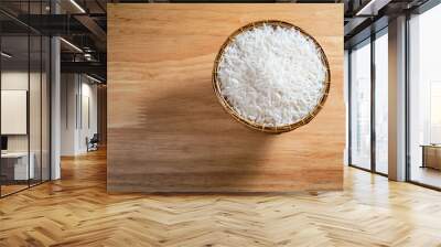 overhead flat lay shot of raw Thai's jasmine rice in Thai's traditional style bamboo's bowl on wooden dinner table with light and shade and some copy space Wall mural