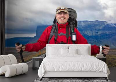 appy bearded tourist with camera, Navigator and trekking poles on road against the mountain landscape in Iceland Wall mural