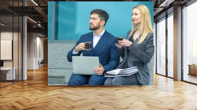 Businessmen partners man and woman on a city street discuss a business project and drink coffee Wall mural