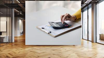 Businesswoman using a calculator to calculate numbers on a company's financial documents, she is analyzing historical financial data to plan how to grow the company. Financial concept. Wall mural