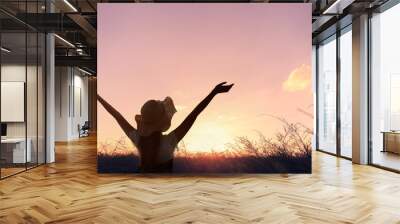 The silhouette of a healthy woman raising her hand on a natural meadow blurred background Wall mural