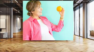 happy pregnant woman holding an orange in her hand on a light blue background. nutrition concept fruit consumption and vitamin c during pregnancy Wall mural