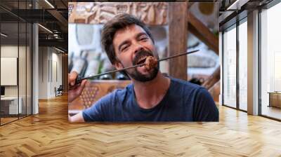 Bearded young man eating meat in a restaurant Wall mural