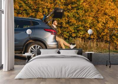 During an autumn afternoon, a man sits in the trunk of a car and enjoys the warmth of the sun Wall mural