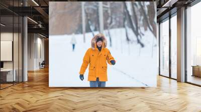 man in yellow winter coat with hood walking by snowed park Wall mural