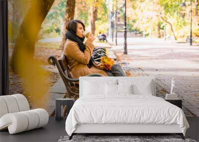 woman sitting on the bench at autumn city park drinking coffee Wall mural