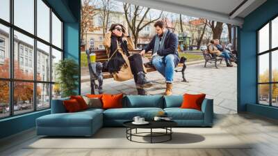 young adult couple eating fast food on bench of city park Wall mural