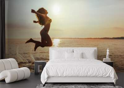 Young Woman Jumps on Beach at sunset Wall mural