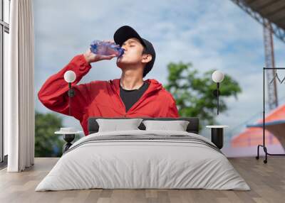 Cool Asian man in sportswear drinking water after exercising in the stadium Asian man drinking water after outdoor jogging at treadmill He exercises and carries a plastic water bottle. active living Wall mural