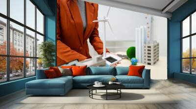 A businesswoman in a brown suit stands at a white desk with a world model, an electric car model, and a green light bulb, promoting Earth Day and sustainable green energy practices. Wall mural