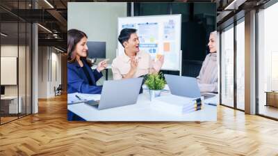 A diverse group of professionals, including a male Asian businessman and a female Muslim businesswoman in hijab, gather around a desk equipped with tablets and laptops for a productive meeting. Wall mural