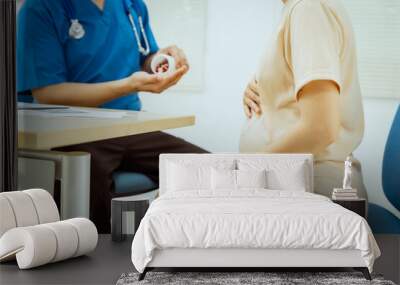 A male Asian pediatrician in a white lab coat conducts a prenatal checkup for a middle-aged pregnant woman, focusing on maternal and fetal health, offering expert care and guidance. Wall mural