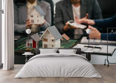 Asian real estate team engaged in a discussion, with two men and a woman focusing on a house model on a table, suggesting a planning or sales meeting. Wall mural