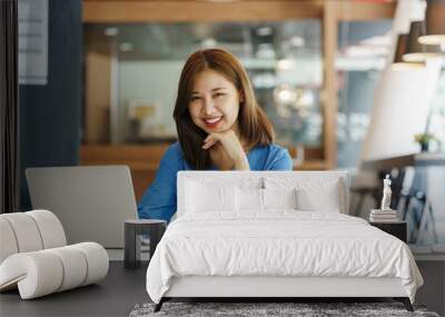 Attractive Asian Young woman freelancer working at the office using a laptop computer Looking at the camera at her comfortable workplace. Wall mural