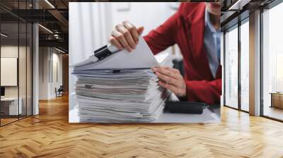 Close up hands of person in a red blazer organizing a substantial stack of various papers, likely sorting or reviewing documents for yearly tax purposes. Wall mural