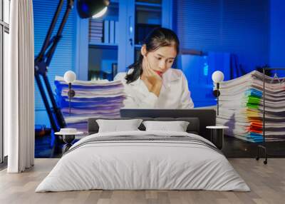 confident Asian businesswoman works late into the night, surrounded by a stack of papers in a busy office. Overtime leads to office syndrome symptoms like neck pain, headaches, and chronic stress. Wall mural