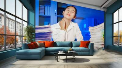 confident Asian businesswoman works late into the night, surrounded by a stack of papers in a busy office. Overtime leads to office syndrome symptoms like neck pain, headaches, and chronic stress. Wall mural