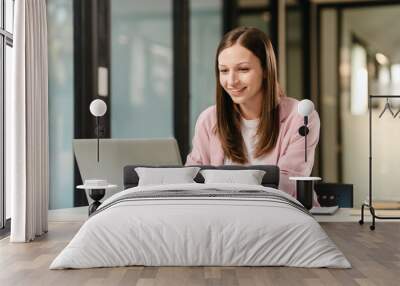 smiling Caucasian university student at a desk with a laptop, likely studying a subject in the humanities. Wall mural