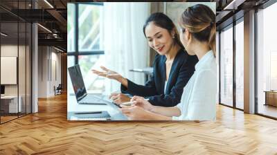 Two young Asian businesswoman discuss investment project working and planning strategy. Business people talking together with laptop computer at office. Wall mural