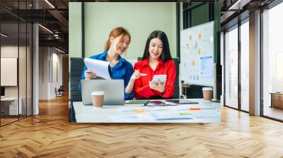 Two young female business consultants work on startup, collaborating on mobile app development social media strategies. whiteboards, documents, they aim to build a successful e-commerce business. Wall mural